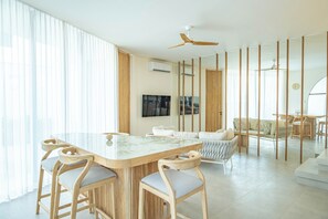 Una sala de estar moderna con una isla de mármol, sillas de madera, un sofá y un ventilador de techo.