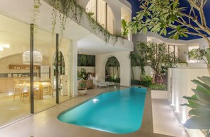 A modern indoor pool area with a clear blue pool, surrounded by plants and seating areas. - Kona Resort Pererenan (Badung)