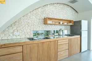 A modern kitchen with a stone wall, wooden cabinetry, and a built-in shelf. - Kona Resort Pererenan (Canggu)