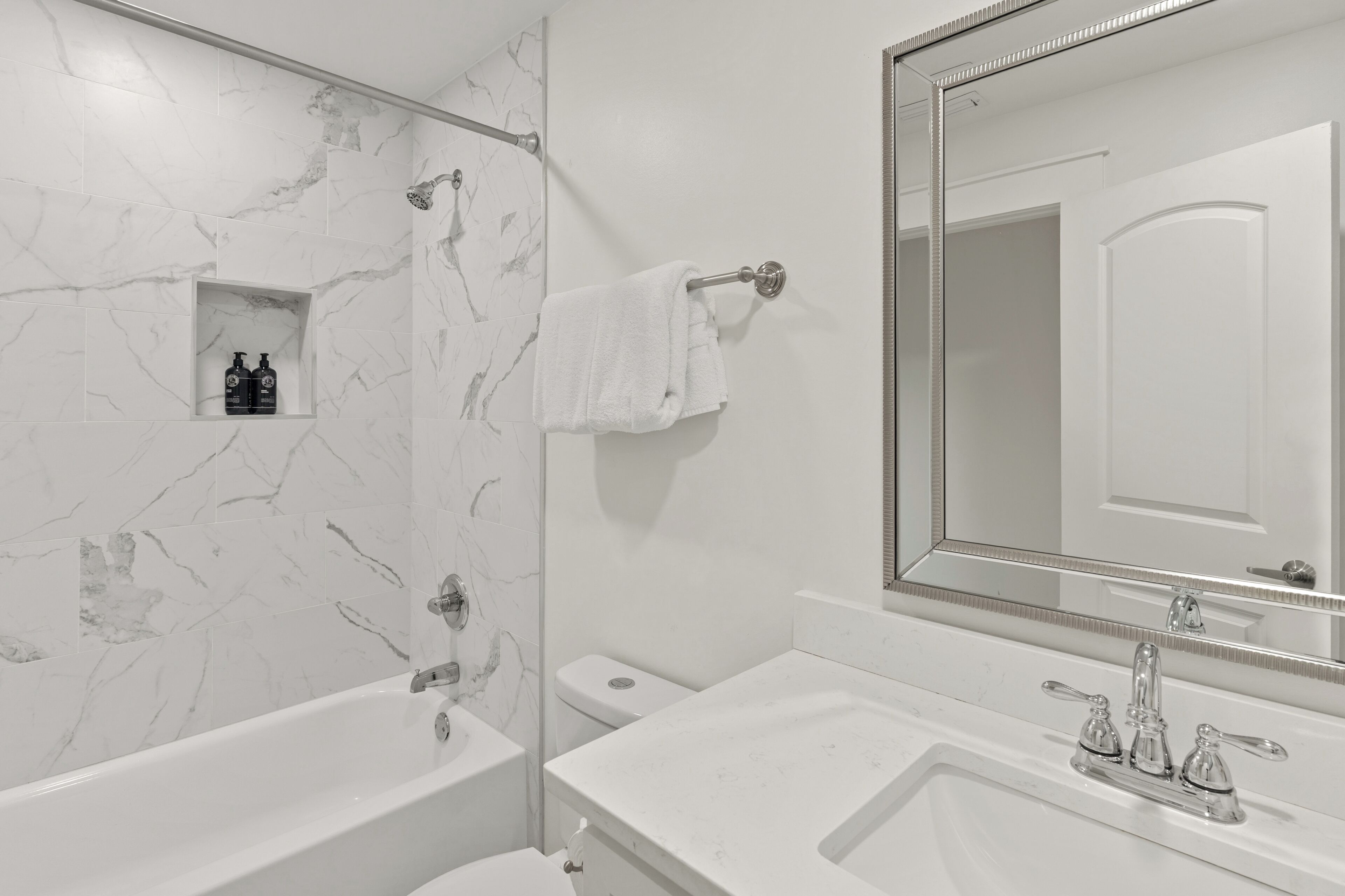 A bathroom with a marble wall, a bathtub, a sink with a mirror, and a towel rack.