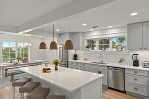 Cocina moderna con una isla grande, electrodomésticos de acero inoxidable e iluminación colgante.