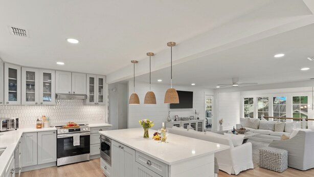A modern kitchen with white cabinetry, a central island, pendant lights, and a dining area with a sofa and table. - Sleeps 18 + Pool + Hot Tub + Wet Bar | Walk to the Beach | The Salty Pearl (Santa Rosa Beach)