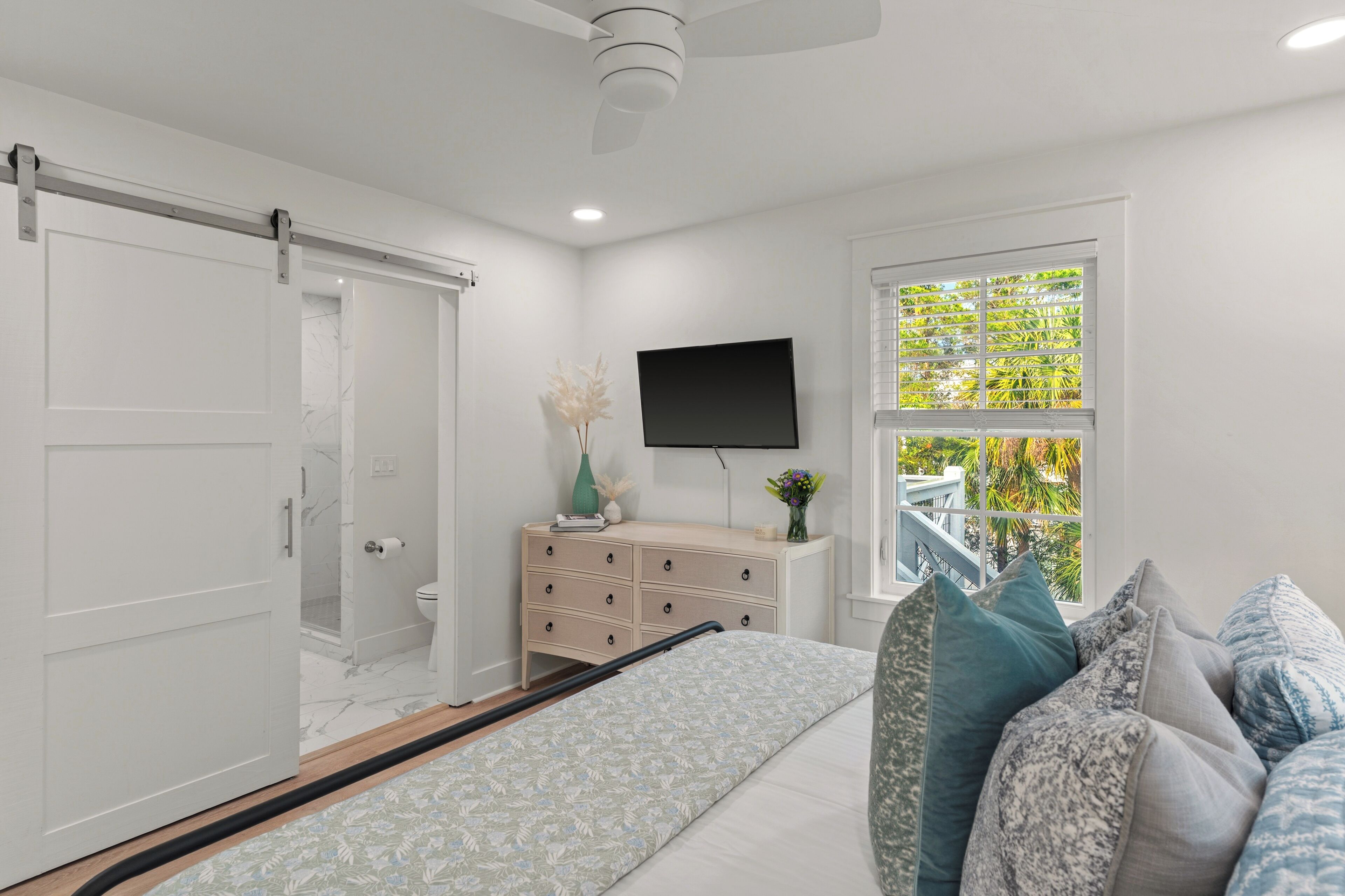 A bedroom with a bed, a dresser, a television, and a window with a view.