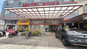 Ein Hotel mit Eingangsbereich und überdachtem Gang, ein Roti O Geschäft und geparkte Fahrzeuge.