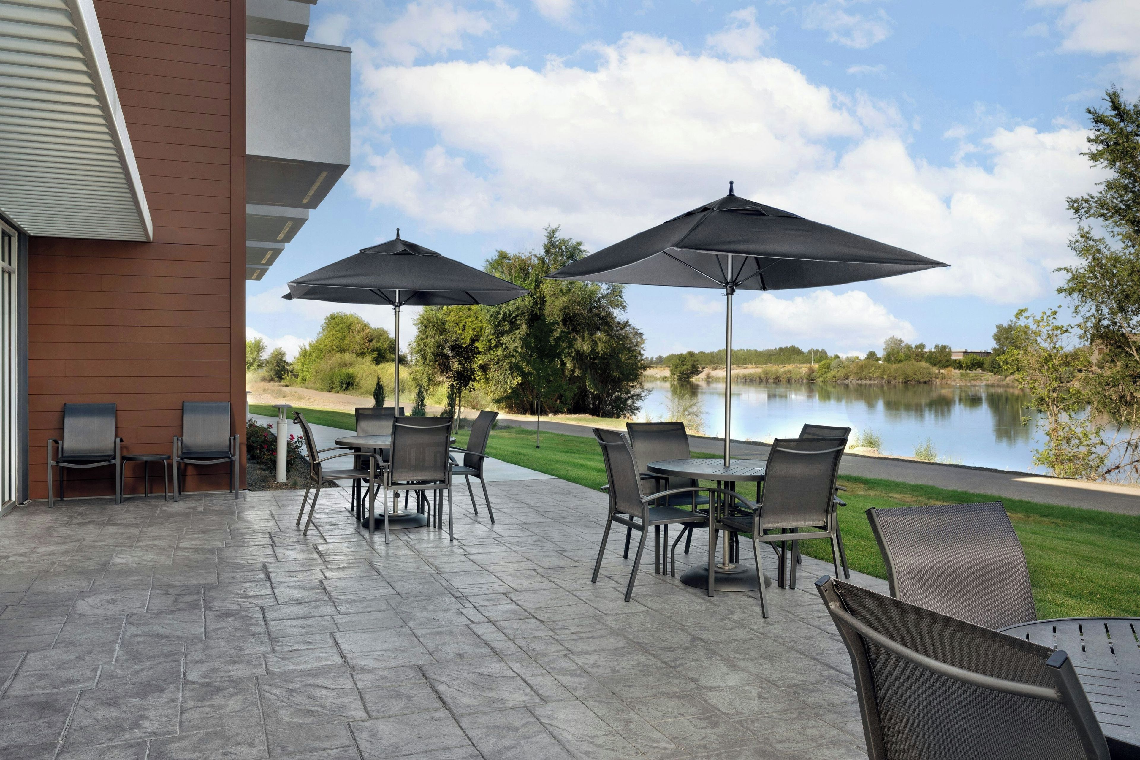 Un patio al aire libre con una mesa, sillas y dos sombrillas, con vista a un lago.