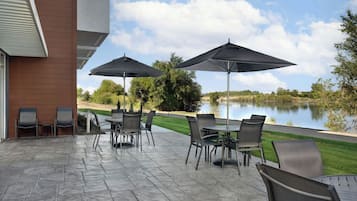 Un patio al aire libre con una mesa, sillas y dos sombrillas, con vista a un lago.