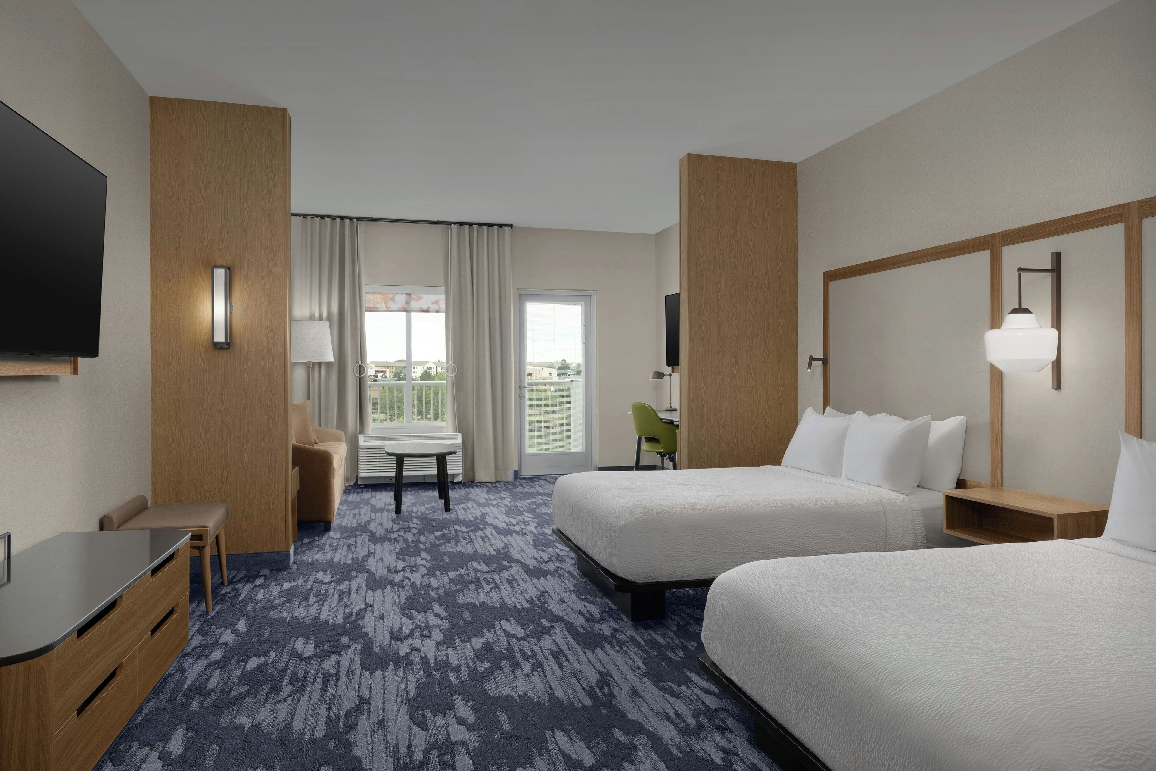 A hotel room with two beds, a desk, a chair, a TV, and a window with curtains.