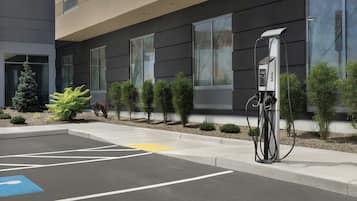 A parking area with a charging station, a blue handicapped parking space, and a building with large windows and a modern design.