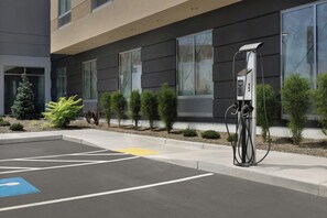 Un espace de stationnement équipé d’une borne de recharge, d’une place de stationnement bleue réservée aux personnes handicapées et d’un bâtiment doté de grandes fenêtres et d’un design moderne.
