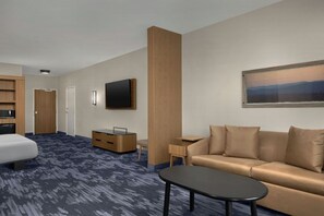 A hotel room with a bed, a sofa, a TV, a desk, and a painting on the wall.