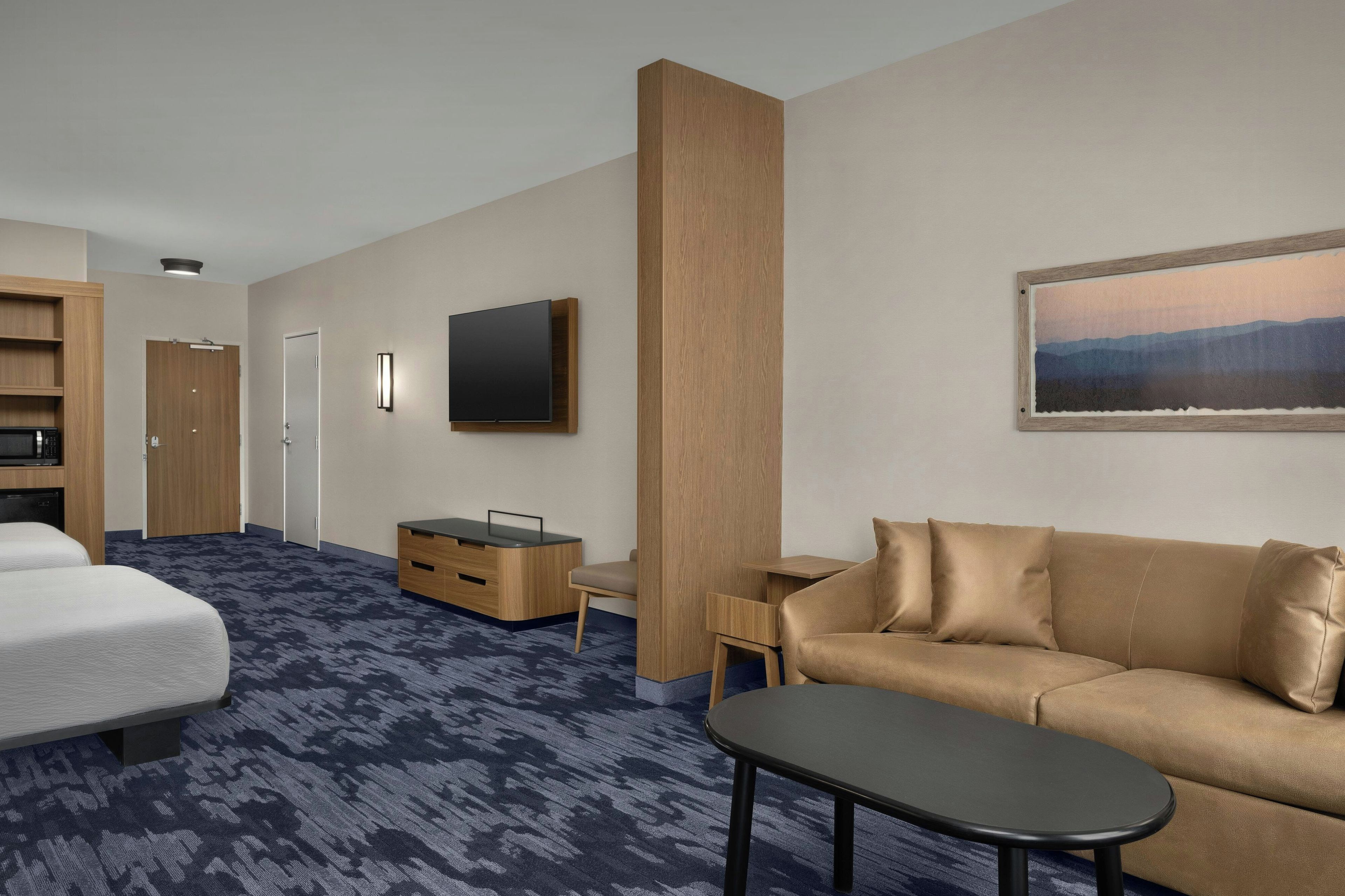 A hotel room with a bed, a sofa, a small table, a TV, a desk, and a painting on the wall.