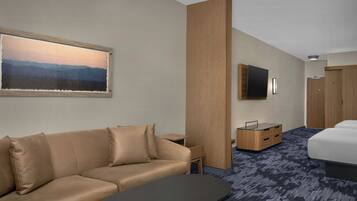 A hotel room with a sofa, a small table, a TV mounted on the wall, a bed, and a wooden wardrobe.