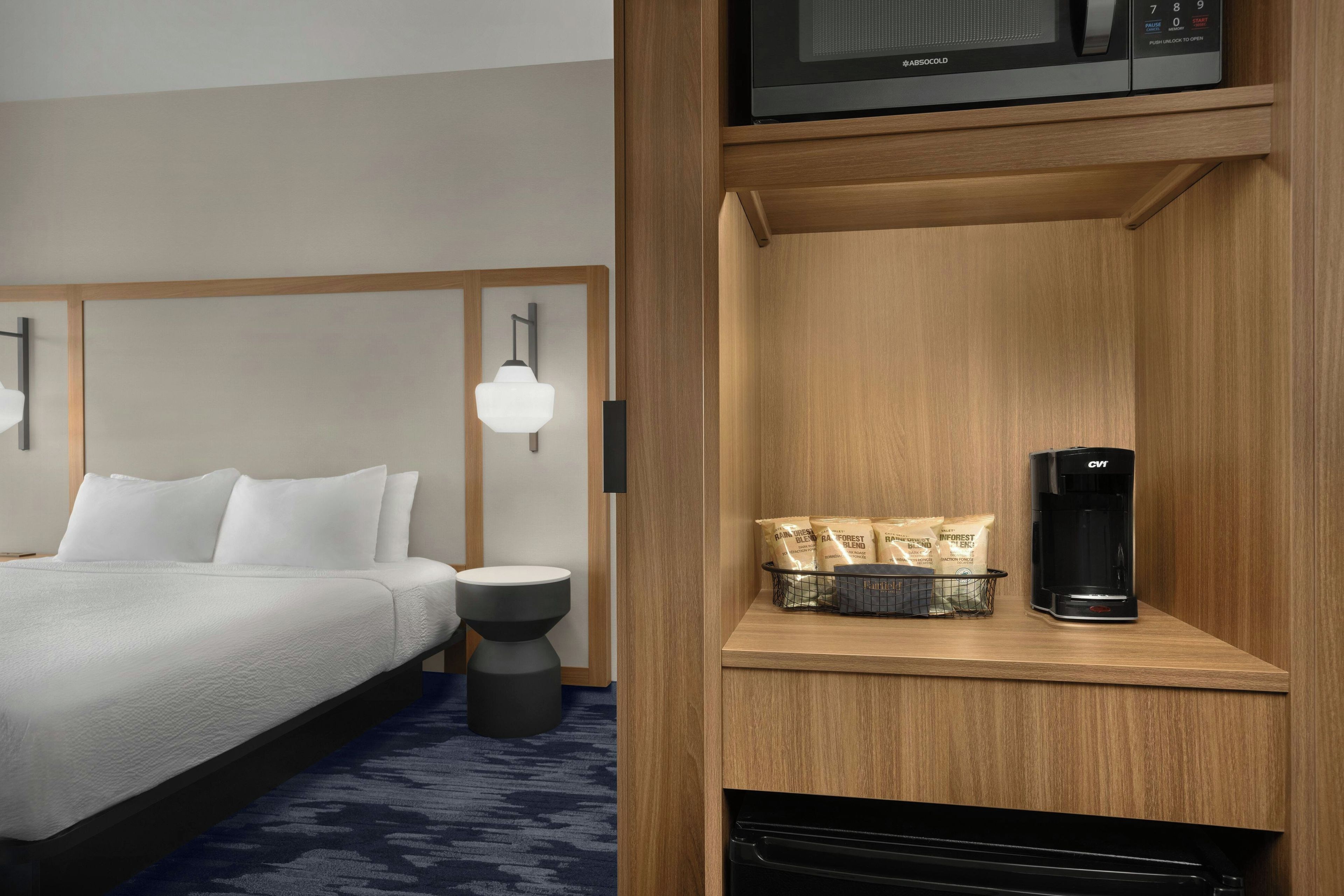 Ett hotellrum med en säng, ett nattduksbord, en lampa och en kaffemaskin placerad på en hylla av trä.