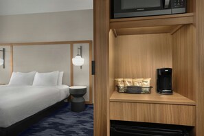 Una habitación de hotel con una cama, mesita de noche, lámpara y una cafetera sobre una estantería de madera.