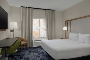 A hotel room with a bed, a desk, a chair, a TV, and a window with curtains.
