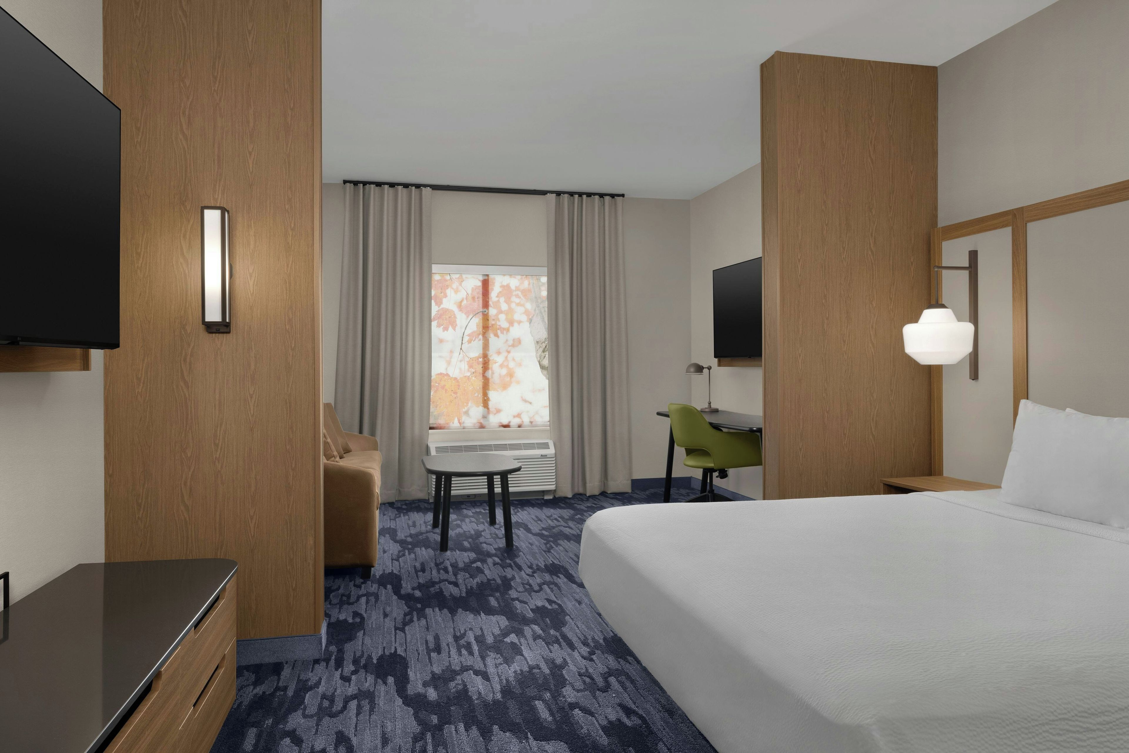 A hotel room with a bed, a desk, a chair, a television, and a window with curtains.