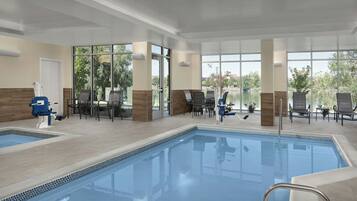 An indoor swimming pool with clear glass walls, lounge chairs, and a view of the outdoors.