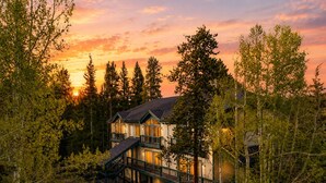 En toetages hytte med balkon, omgivet af tæt skov i solnedgang.