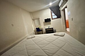 Une chambre à coucher avec un lit, un bureau, une chaise, une télévision et une fenêtre.