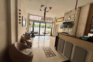 Un hall d’hôtel avec des meubles en osier, un sol carrelé, un comptoir de réception et un téléviseur fixé au mur.