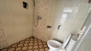 A bathroom with a patterned floor, a toilet, a shower, and a wall-mounted towel dispenser. - Poma Zainoel Deluxe Twin (Banda Aceh)