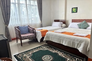 A hotel room with two beds, a chair, a desk, and a patterned rug.