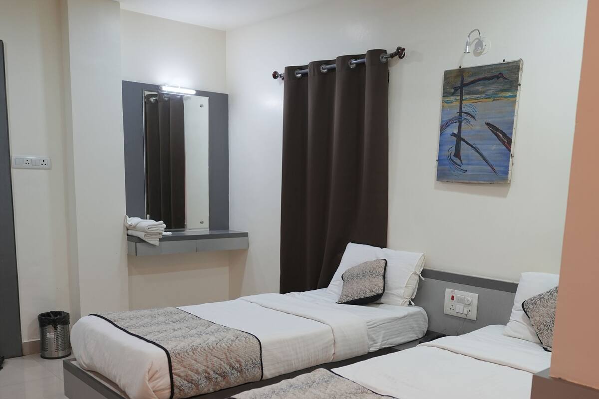 Quarto de hotel com duas camas, um ventilador de teto, um quadro e uma pequena lixeira.