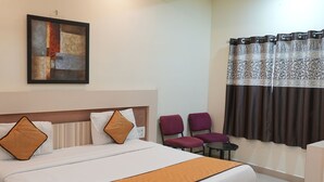 Een hotelkamer met een bed, een plafondventilator, een schilderij, een raam met gordijnen en twee stoelen.