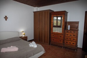 Un dormitorio con una cama, un armario de madera, un tocador y una cruz en la pared.