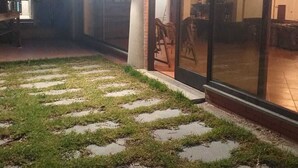 Un edificio con amplios ventanales, un espacio exterior pavimentado con piedras y un interior visible con muebles.