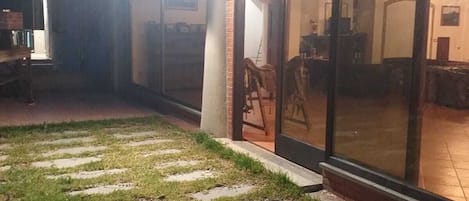 A building with large glass doors, a paved outdoor area with stepping stones, and a visible interior with furniture.