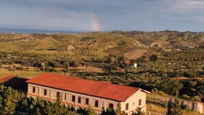 Paisaje rural con colinas ondulantes, un edificio con techo de tejas rojas y un arcoíris a lo lejos.