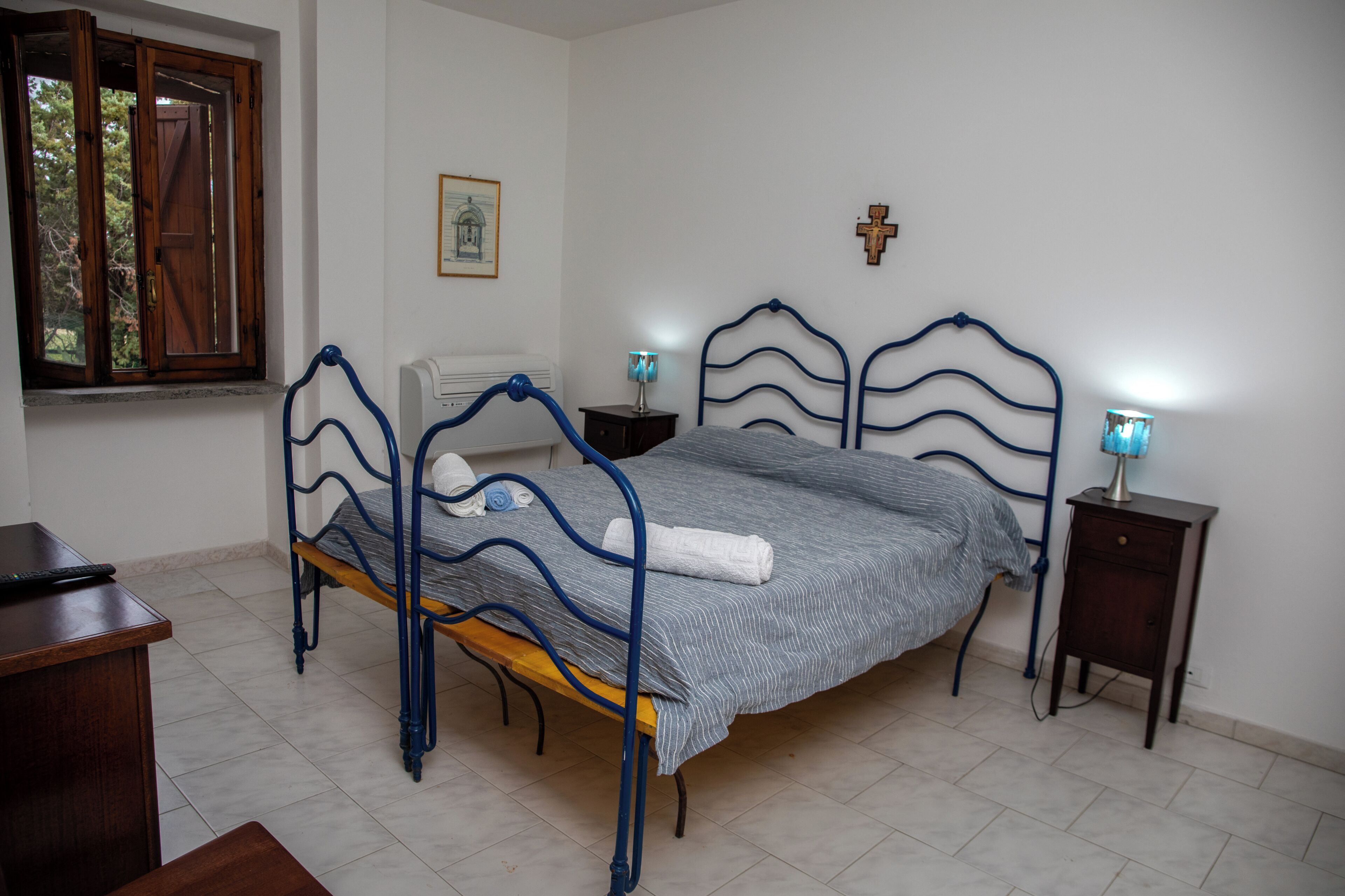 Une chambre à coucher avec un lit, des tables de chevet, une fenêtre et une croix accrochée au mur.