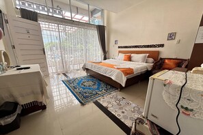 A bedroom with a bed, a desk, a chair, a refrigerator, and a window with curtains.