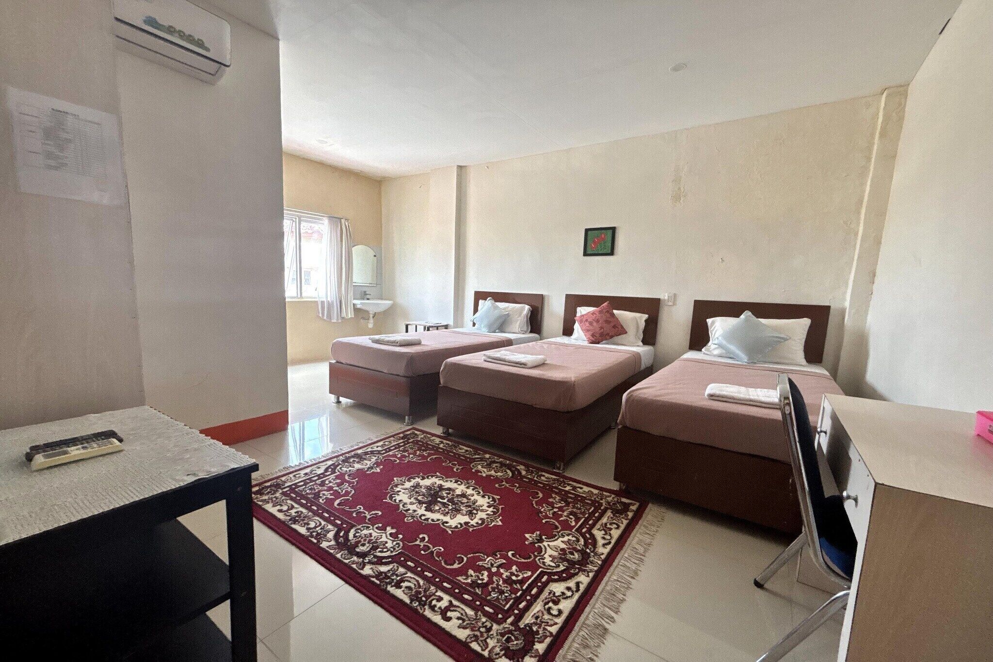 A hotel room with two beds, a desk, a chair, a small table, a rug, and a window.