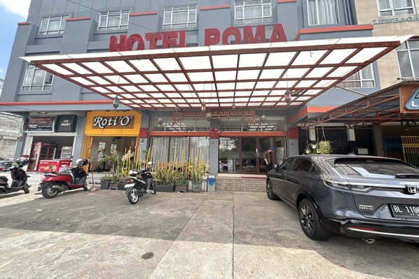 A hotel entrance with a covered walkway, a Roti O shop, and parked vehicles.