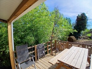 A wooden deck with a picnic table and chairs, surrounded by lush greenery.