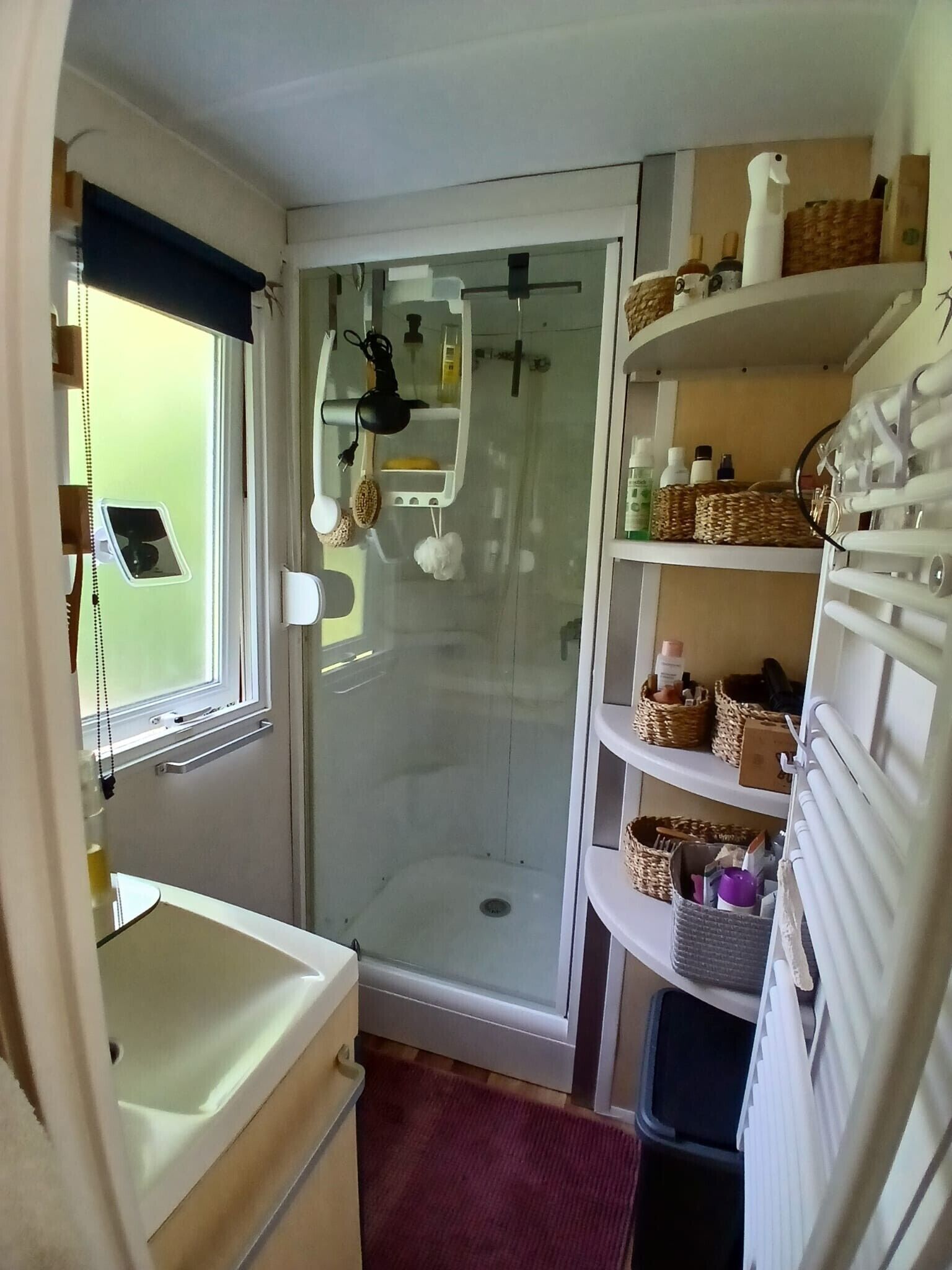 Casa de banho compacta com chuveiro, lavatório e prateleiras com cestos.