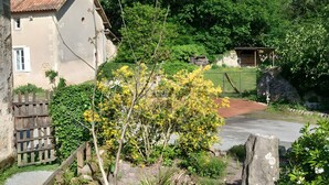 Un bâtiment rustique, doté d’un toit en tuiles, entouré d’une végétation luxuriante et d’un petit étang.