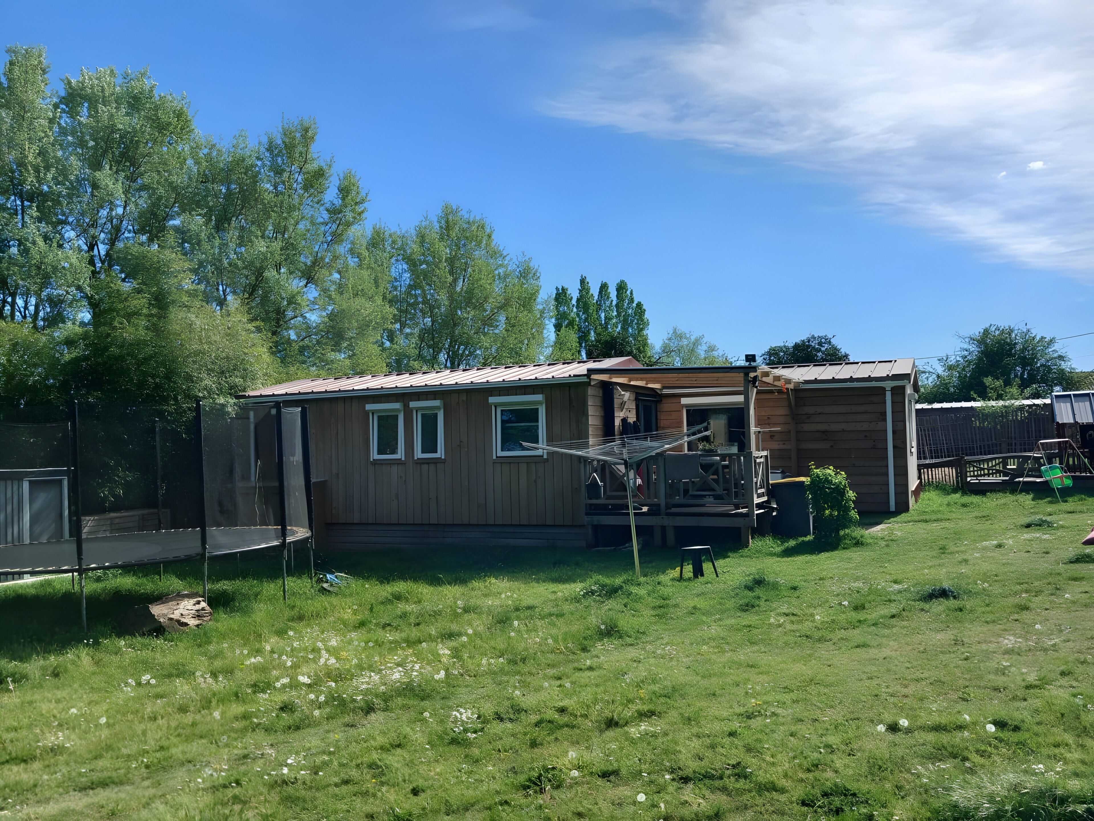 Une cabane en bois avec une véranda, une cour clôturée et un trampoline.