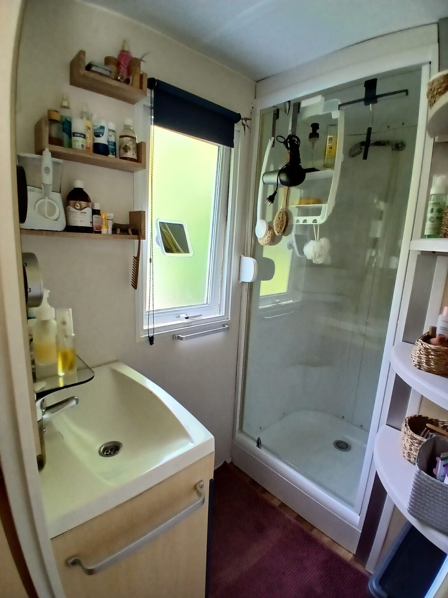 Ein kleines Badezimmer mit Dusche, Waschbecken und Regalen für Pflegeprodukte.