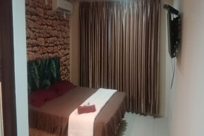 Une pièce avec un lit, un mur en pierre, un rideau et un appareil fixé au mur.