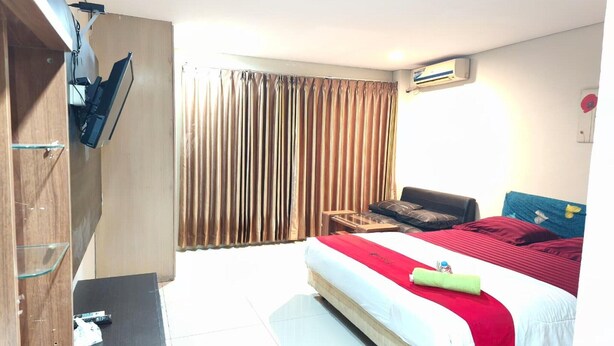 A hotel room with a bed, a desk, a chair, a wardrobe, and a window with curtains. - Barkah Balikpapan Deluxe Double (Balikpapan)