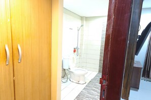 Une salle de bain avec des toilettes, une douche et une porte en bois.