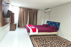 Une chambre à coucher avec un lit, des rideaux, un téléviseur fixé au mur et une petite table de chevet.