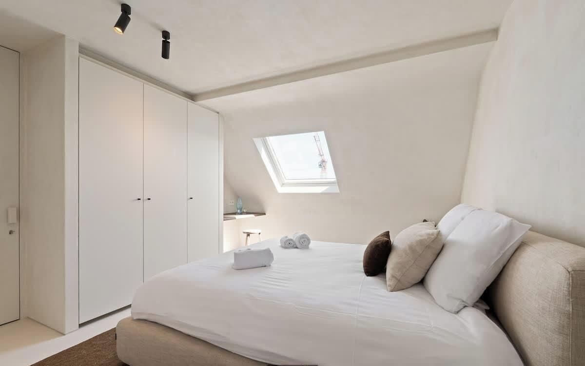 A bedroom with a skylight, a bed with pillows, a bedside table, and a wardrobe.