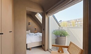 Ein Schlafzimmer mit einem Bett, einer Topfpflanze und einem Fenster mit Blick auf eine Skyline.