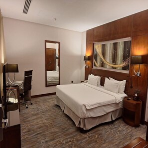A hotel room with a large bed, a desk with a chair, a mirror, and a painting on the wall. - Exclusive Club Suite Sunday Qaser Al Hamra (Riyadh)