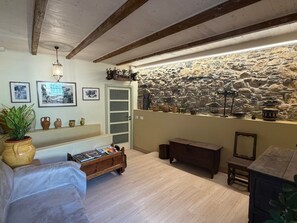 A room with a stone wall, wooden beams, a bed, a wooden bench, a small table, and a shelf with decorative items. - Apartment 'Rosmarino' with Sea View, Wi-Fi, and Air Conditioning (Moglio)