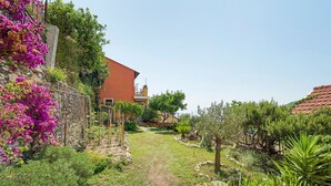 A garden path leading to a building with a red roof, surrounded by various plants and a stone wall. - Apartment 'Rosmarino' with Sea View, Wi-Fi, and Air Conditioning (Moglio)